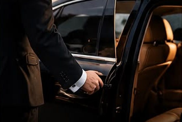 Chauffeur in a dark suit opening a car door to a tan leather interior